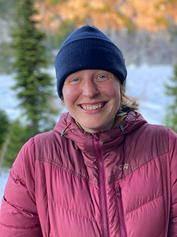 Person smiles at the camera. They are wearing a warm hat and jacket.